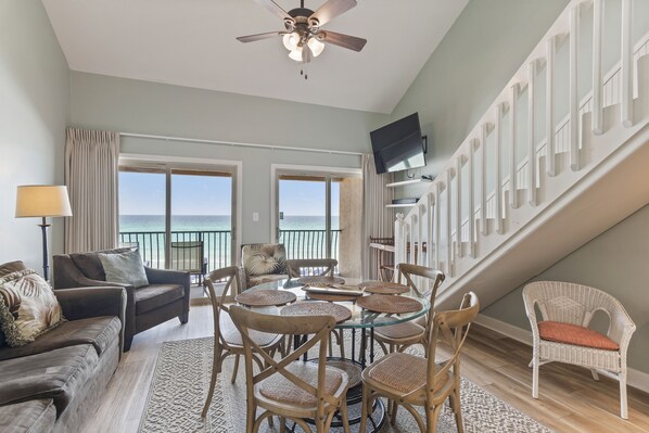 A spacious living area with a balcony overlooking the sea, furnished with a sofa, chairs, and a dining table. - 38- Quaint, family friendly, 3 story condo on the gorgeous EMERALD COAST! (Destin)