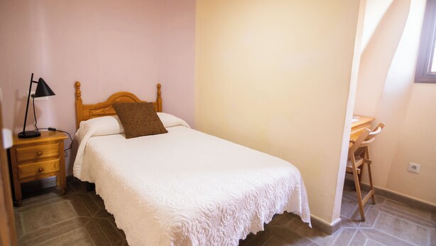 Un dormitorio con cama, mesita de noche, lámpara y una silla.
