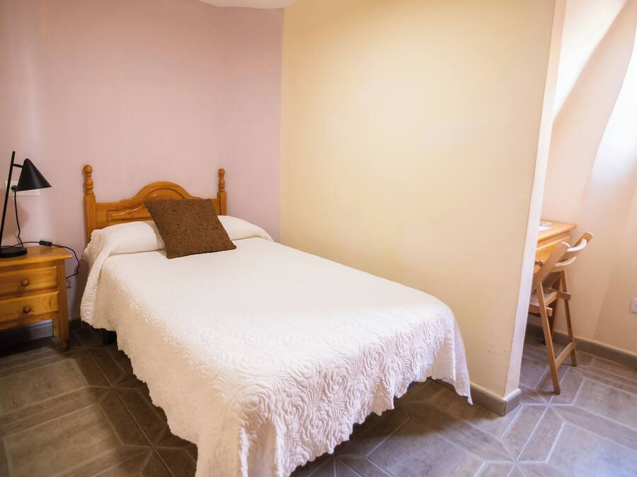 A bedroom with a bed, a nightstand, a lamp, and a chair.