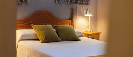 Una cama con cabecera de madera, dos almohadas, una lámpara de noche y una colcha estampada.