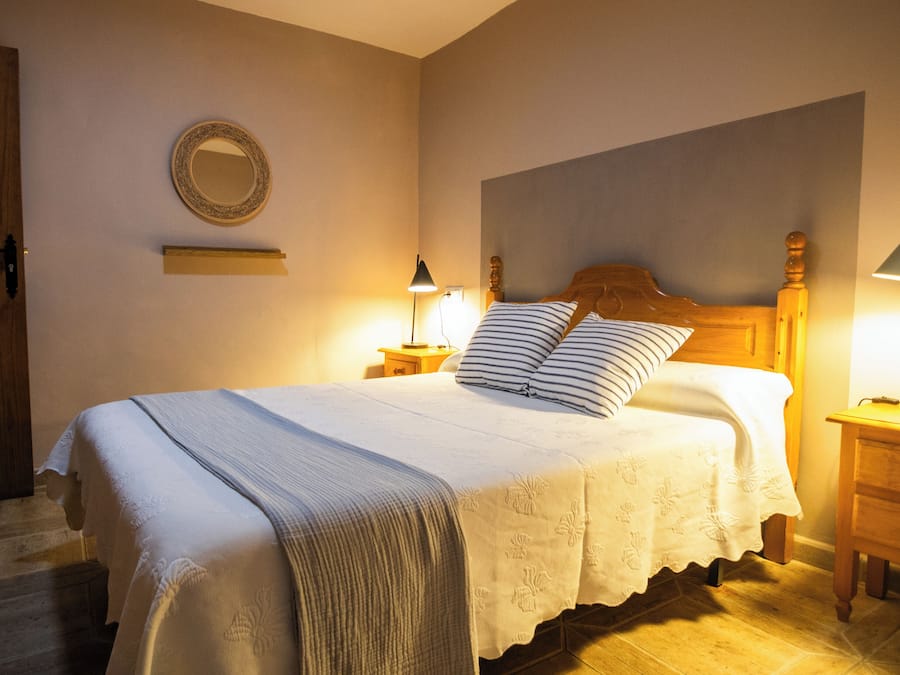 Un dormitorio con una cama, una mesita de noche, una lámpara, un espejo y una puerta de madera.