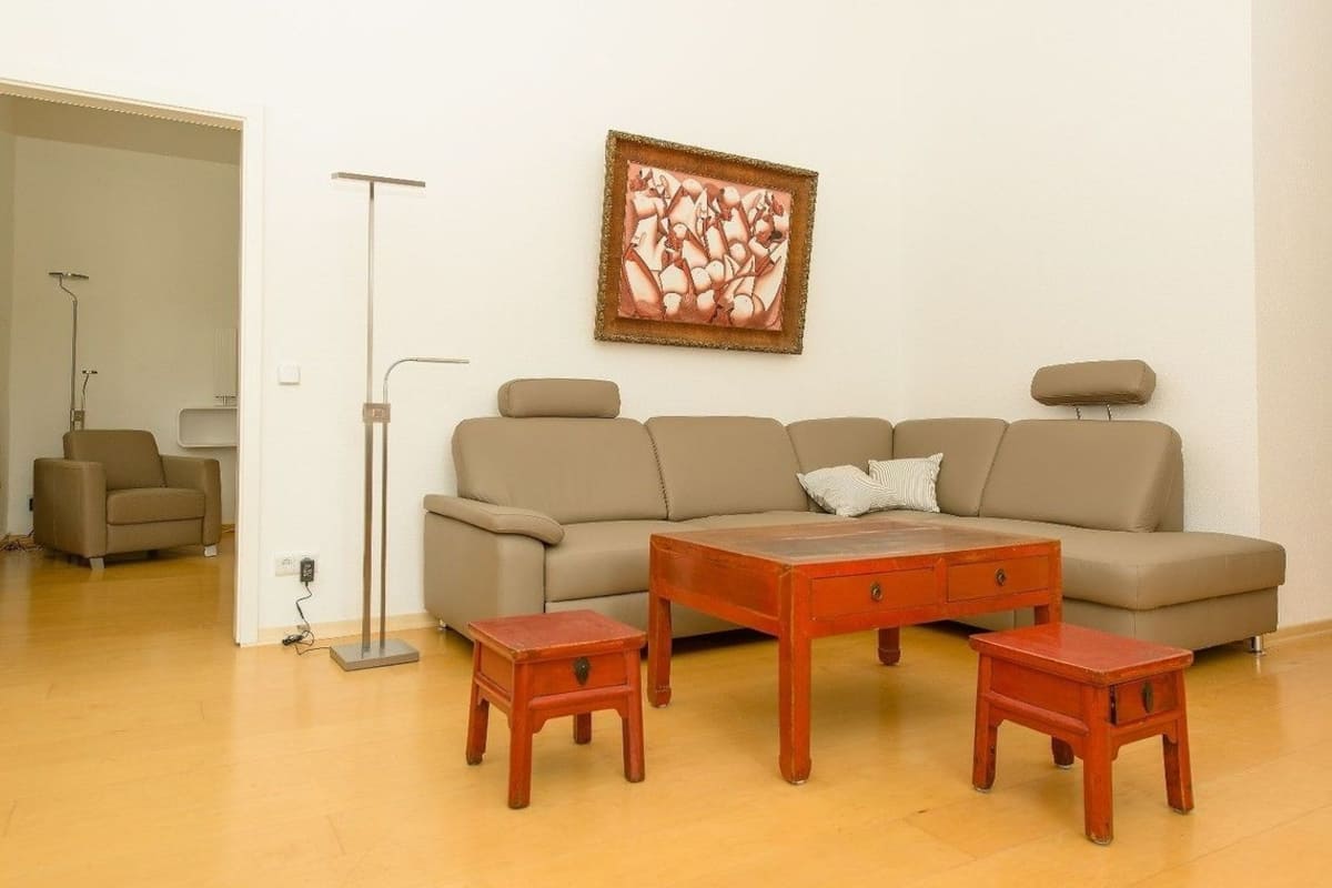 Un salon comprenant un canapé, deux petites tables en bois, une lampe sur pied et une œuvre d’art encadrée accrochée au mur.