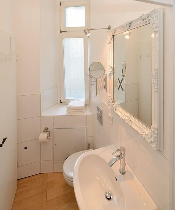 Un baño pequeño y moderno con lavamanos, espejo y retrete blancos.