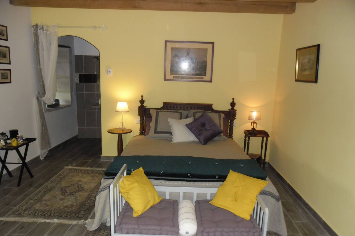 Une chambre à coucher avec un lit, deux tables de chevet, une commode, une fenêtre avec un rideau et un tableau encadré au mur.