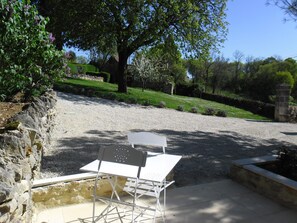 An outdoor seating area with a table and chairs, surrounded by a stone wall and a grassy hill. - Bergerie de Lagarrigue (Baladou)