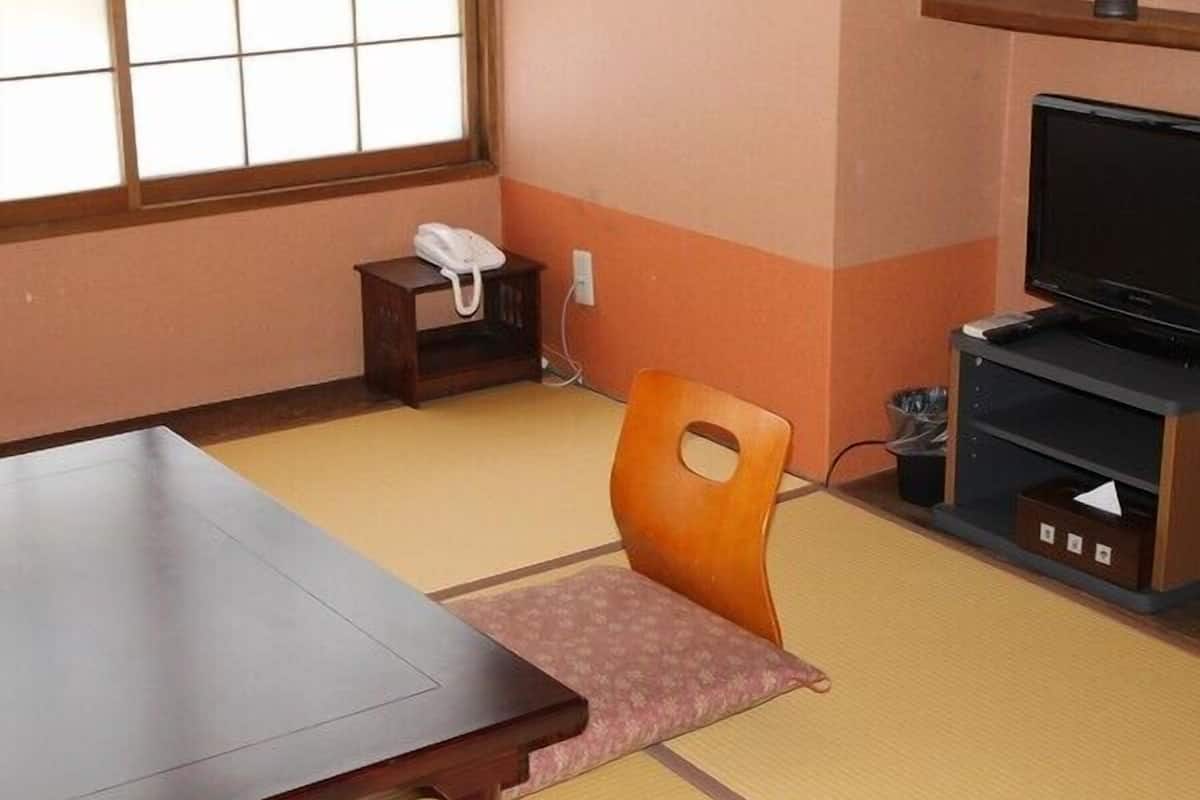 Una habitación con suelo de tatami, una mesa de madera, una silla, un televisor y un teléfono sobre una mesita.