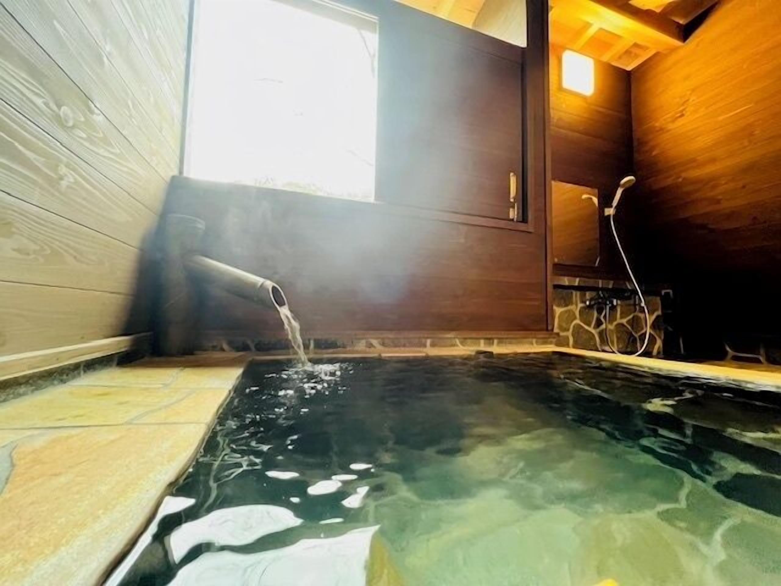 Un bain thermal, avec un intérieur en bois, un mur en pierre et une fenêtre laissant entrer la lumière naturelle.