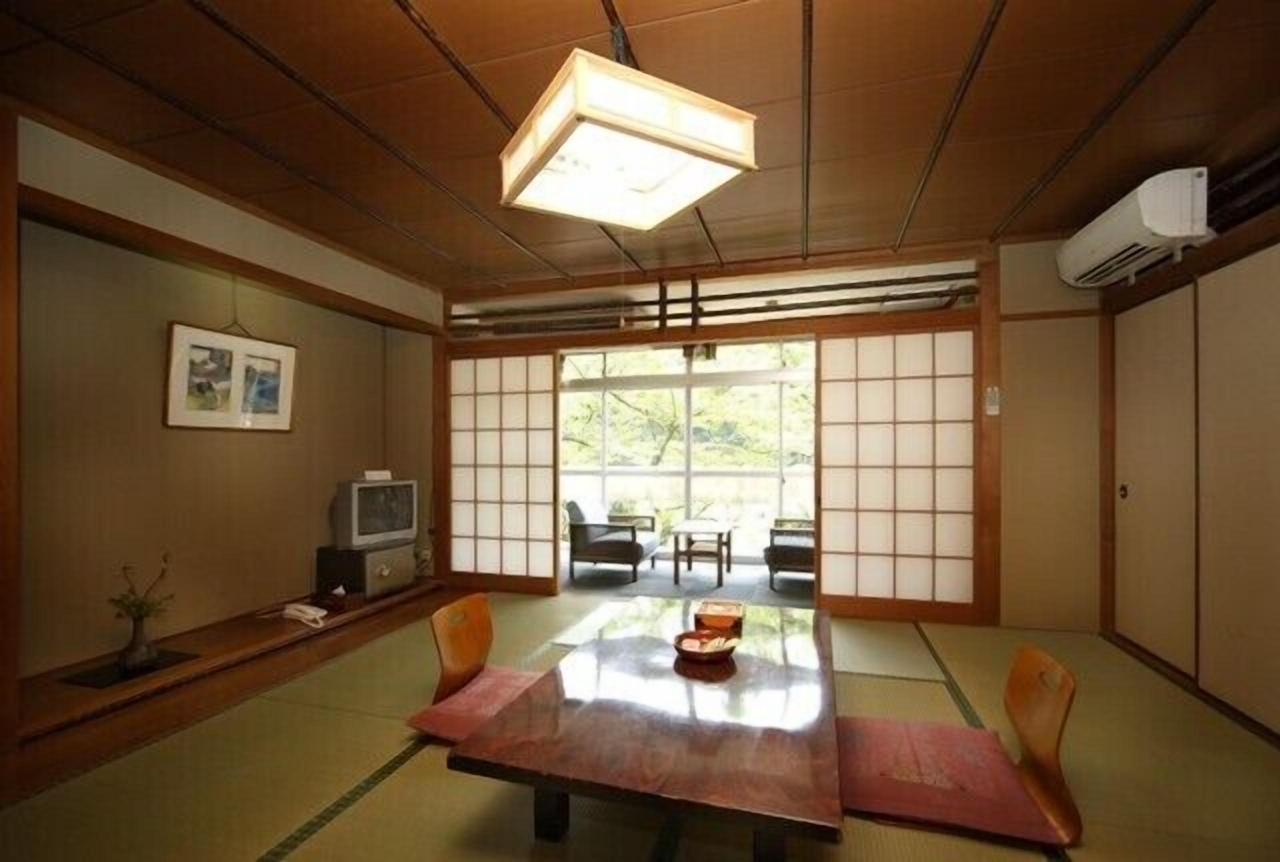 A traditional Japanese room with tatami flooring, a low table with cushions, sliding doors, and a television.