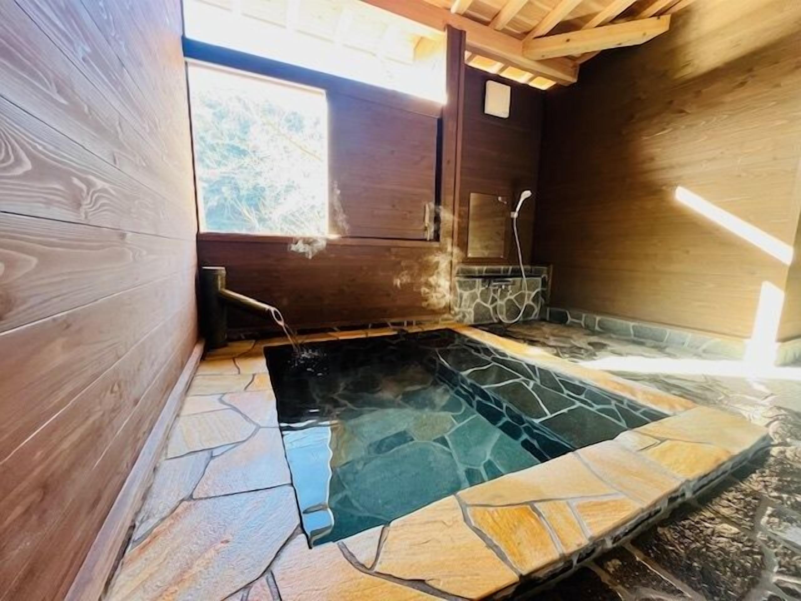 A hot spring bath with stone flooring, wooden walls, and a wooden ceiling structure.