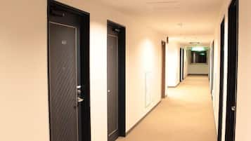 A hotel corridor with dark doors, a light-colored carpet, and a long, straight layout.