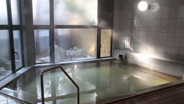 Een wellnessruimte met een warmwaterbron, een glazen wand, een metalen leuning en een betegelde vloer.