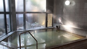 A hot spring bath area with a glass partition, a metal railing, and a tiled floor. - Yuda Onsen Hotel Kiraku (Yamaguchi)