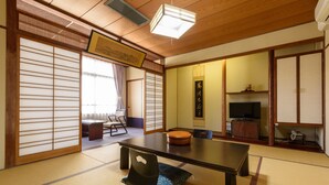 Een traditionele Japanse kamer met tatami vloerbedekking, een lage tafel, een stoel, schuifdeuren, een televisie en een klein kastje.