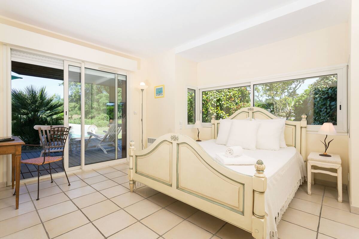 Un dormitorio con cama, una silla, una mesa y un ventanal corredero que da a un balcón.