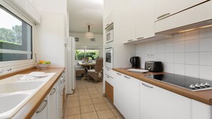 Une cuisine moderne avec des armoires blanches, un plan de travail en bois, un évier, une cuisinière et un coin repas comprenant une table et des chaises.