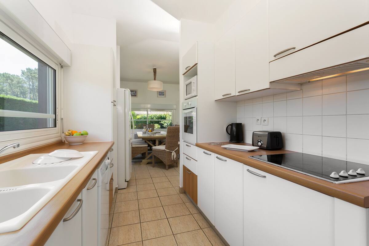 Una cocina moderna con armarios blancos, encimera de madera, un fregadero, una estufa y un comedor con mesa y sillas.
