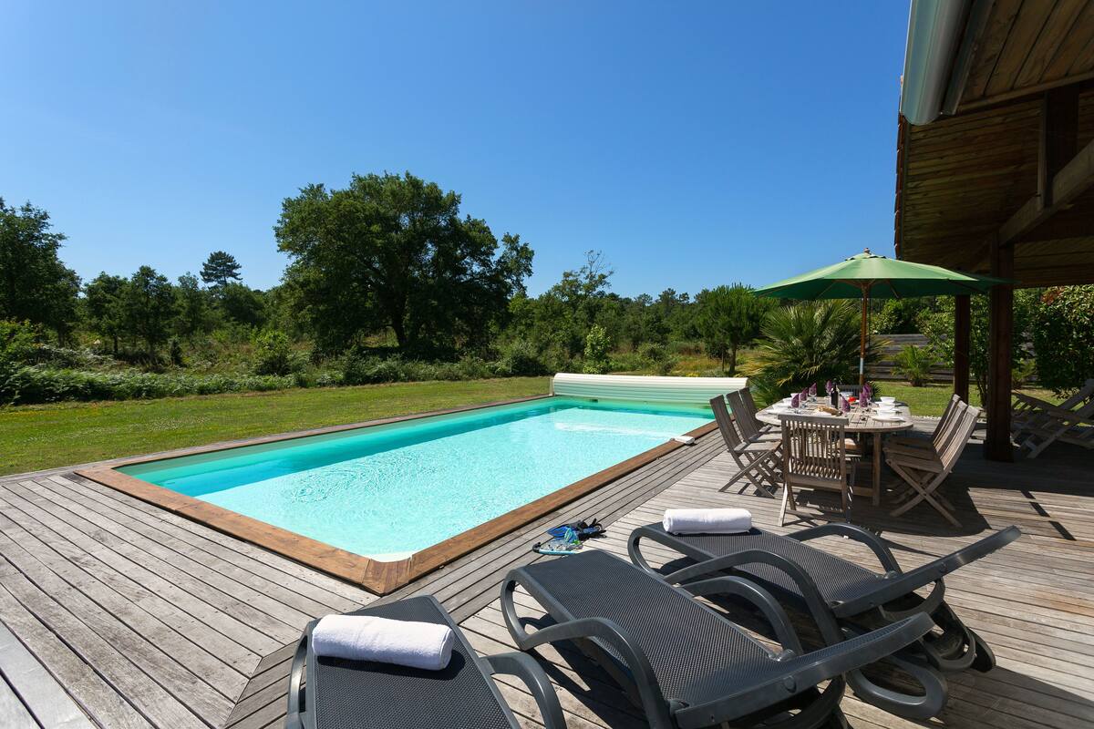 Una terraza de madera con piscina, sillas de descanso y una mesa con sombrillas.