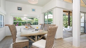 Un coin repas avec une table en bois, des chaises en osier et une vue sur le jardin grâce à de grandes fenêtres.
