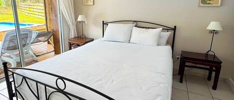 A bedroom with a bed, two bedside tables, a chair, and a view of a pool.