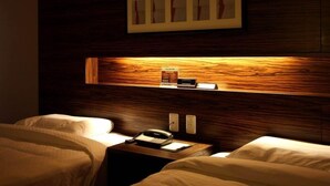 A hotel room with a wooden headboard, a bedside table with a telephone and a book, and a framed picture above the headboard. - International Hotel Ube (Ube)