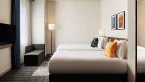 Ein Hotelzimmer mit zwei Betten, einem Fernseher, einem Sofa und einer Lampe.