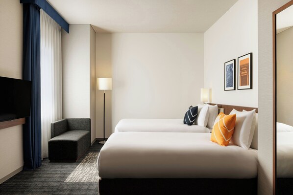 Habitación de hotel con dos camas, televisor, sofá y lámpara.