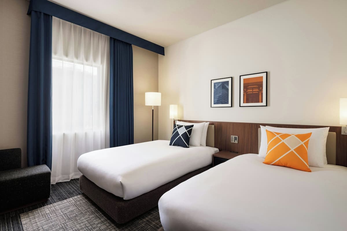 A hotel room with two beds, a desk, a chair, and a window with curtains.
