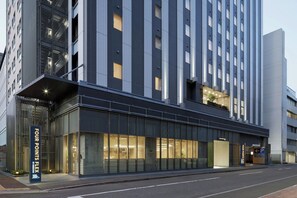 Un hotel moderno con fachada de vidrio, un llamativo letrero de 'FOUR POINTS FLEX' y un letrero de 'ROOK HOUSE' que indica un restaurante.