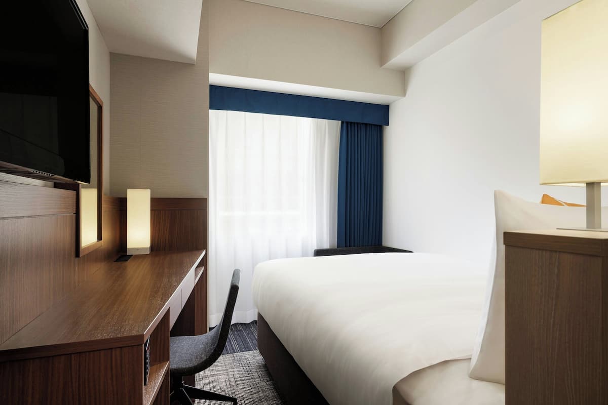 A hotel room with a bed, a desk, a chair, a television, and a window with curtains.