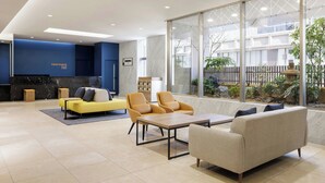 Eine moderne Lobby mit Empfangstresen, Sitzgelegenheiten und großen Fenstern mit Blick ins Freie.