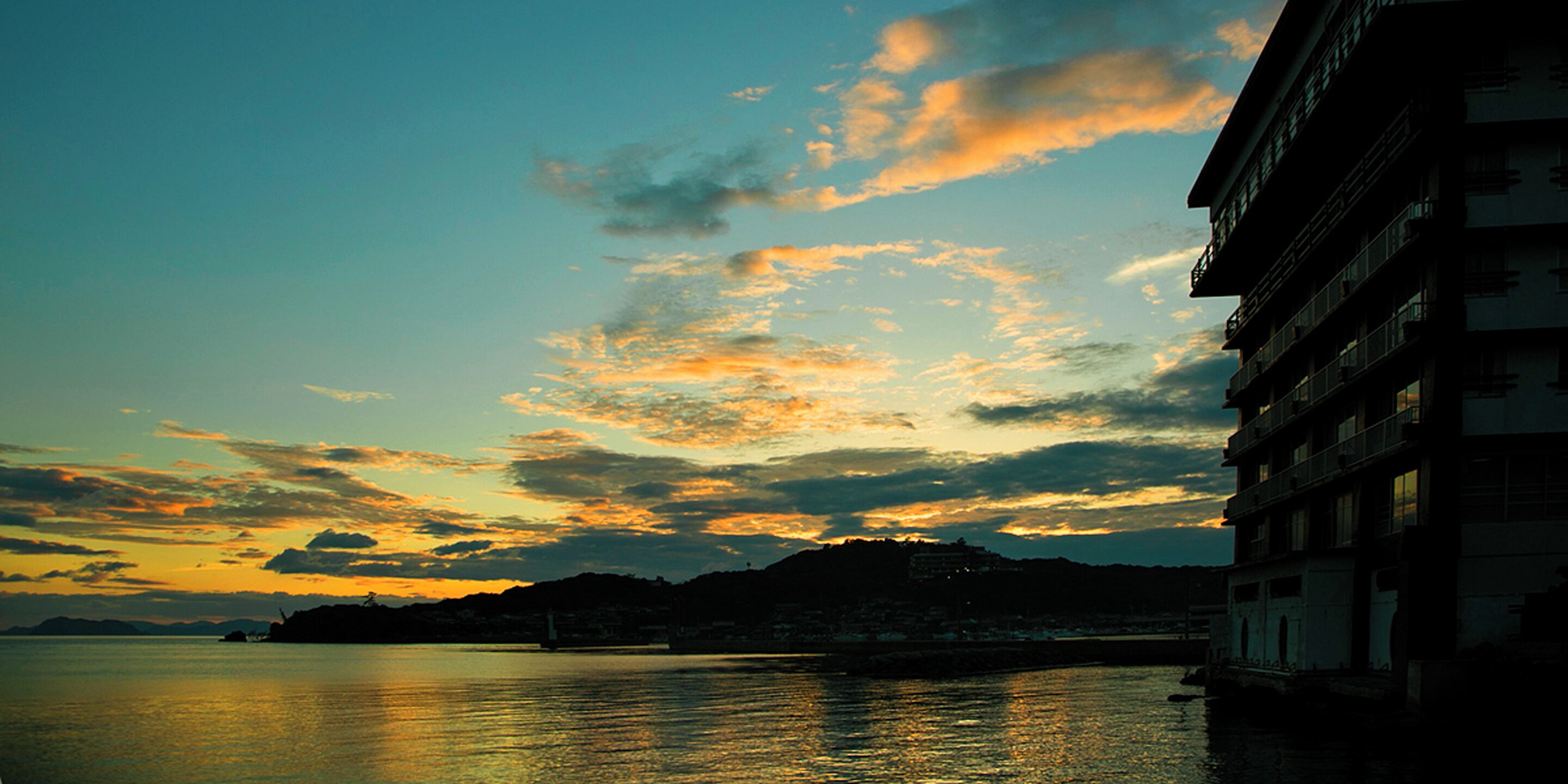 A coastal view with a building on the right and a sunset in the background.