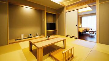 A traditional Japanese-style room with tatami flooring, a low wooden table, a television, and sliding doors leading to a bedroom.