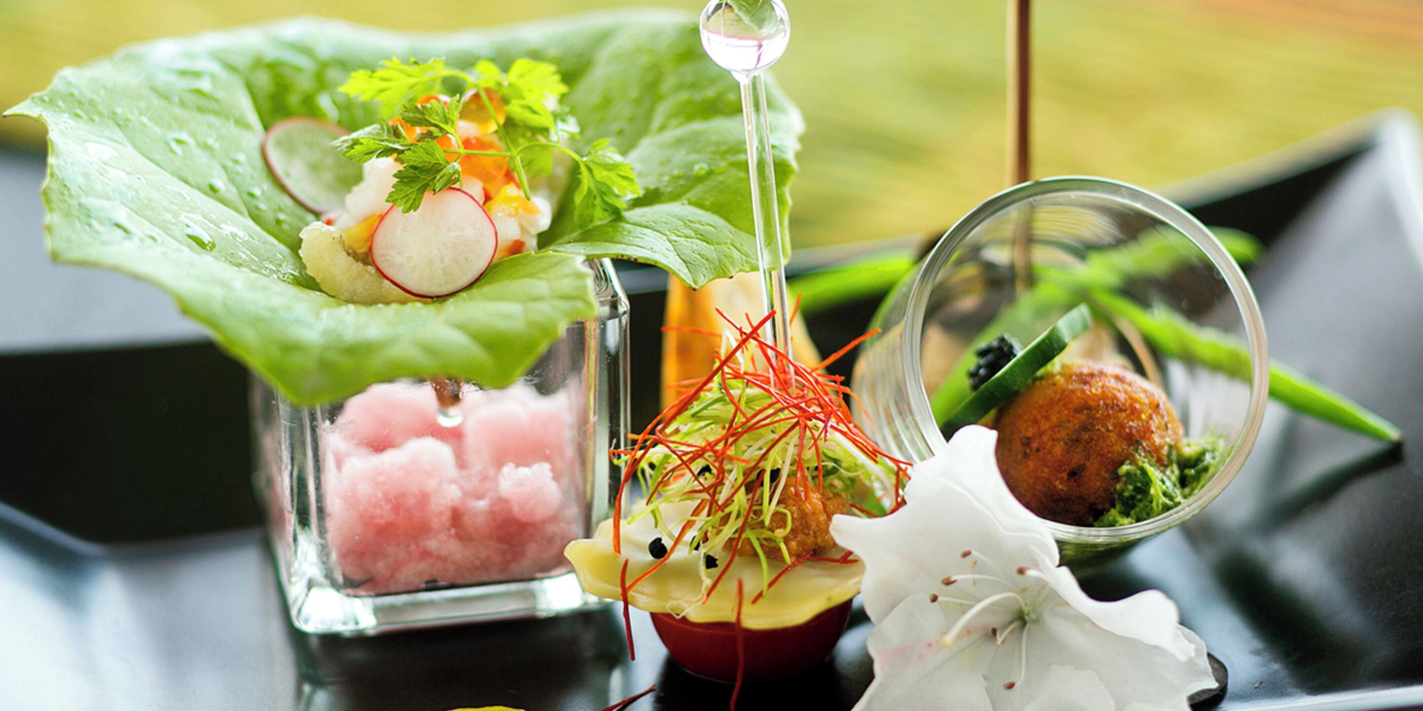 A variety of dishes including sushi, a salad, and a meatball, presented on a table with a green leaf garnish.