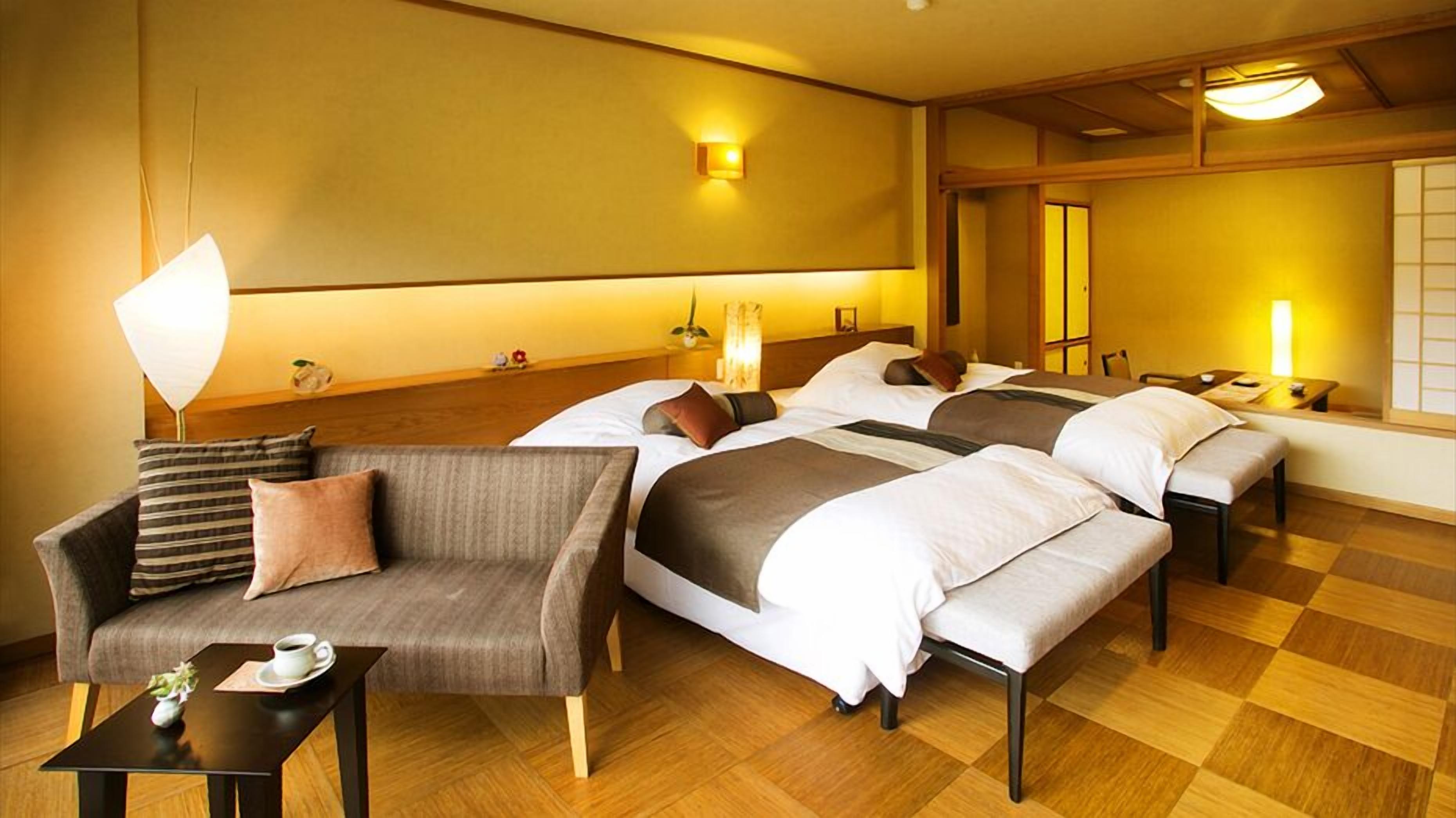 A hotel room with a sofa, two beds, a small table with a cup, and a lamp.