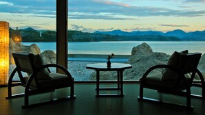 Een kamer met twee stoelen gericht op een tafel, een grote zuil en uitzicht op een meer en bergen.