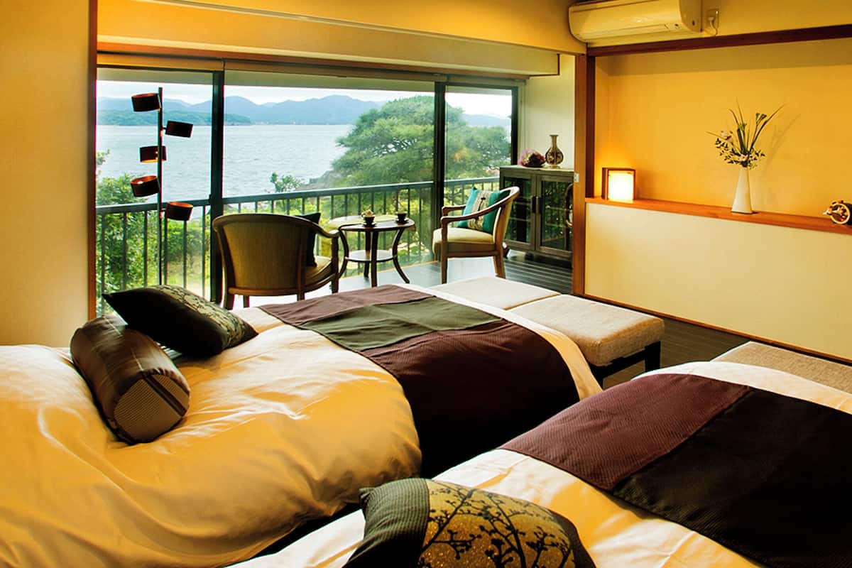 Ein Hotelzimmer mit zwei Betten, einem Balkon mit Meerblick, einem kleinen Tisch und einem Sessel.