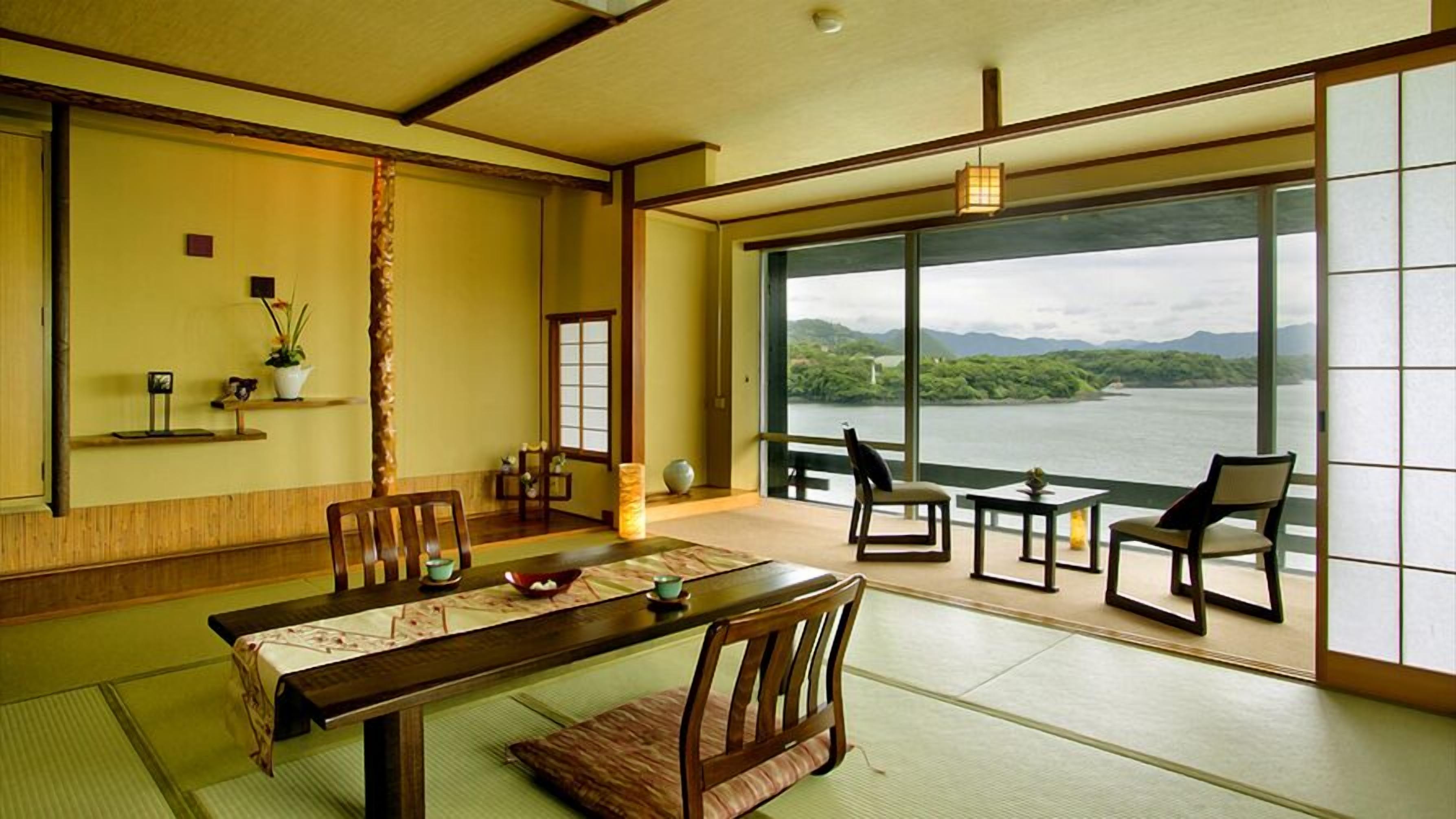 Una tradizionale stanza giapponese con pavimento in tatami, un tavolino, sedie, vista su un lago e una porta scorrevole.
