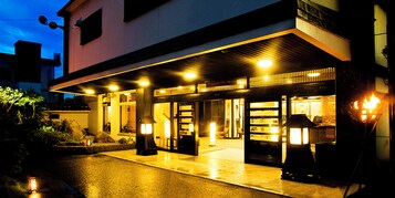 Entrada de hotel con un corredor cubierto, iluminada por varias luces y un farol tradicional japonés.
