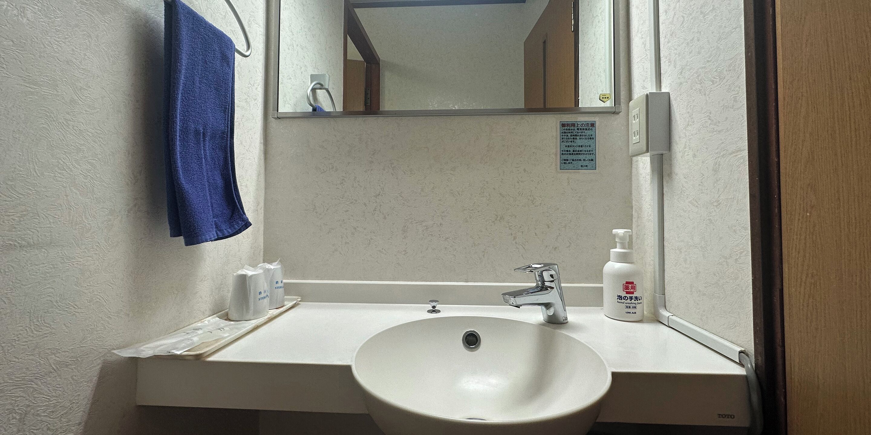 A bathroom with a white sink, a mirror, a blue towel, and a soap dispenser.
