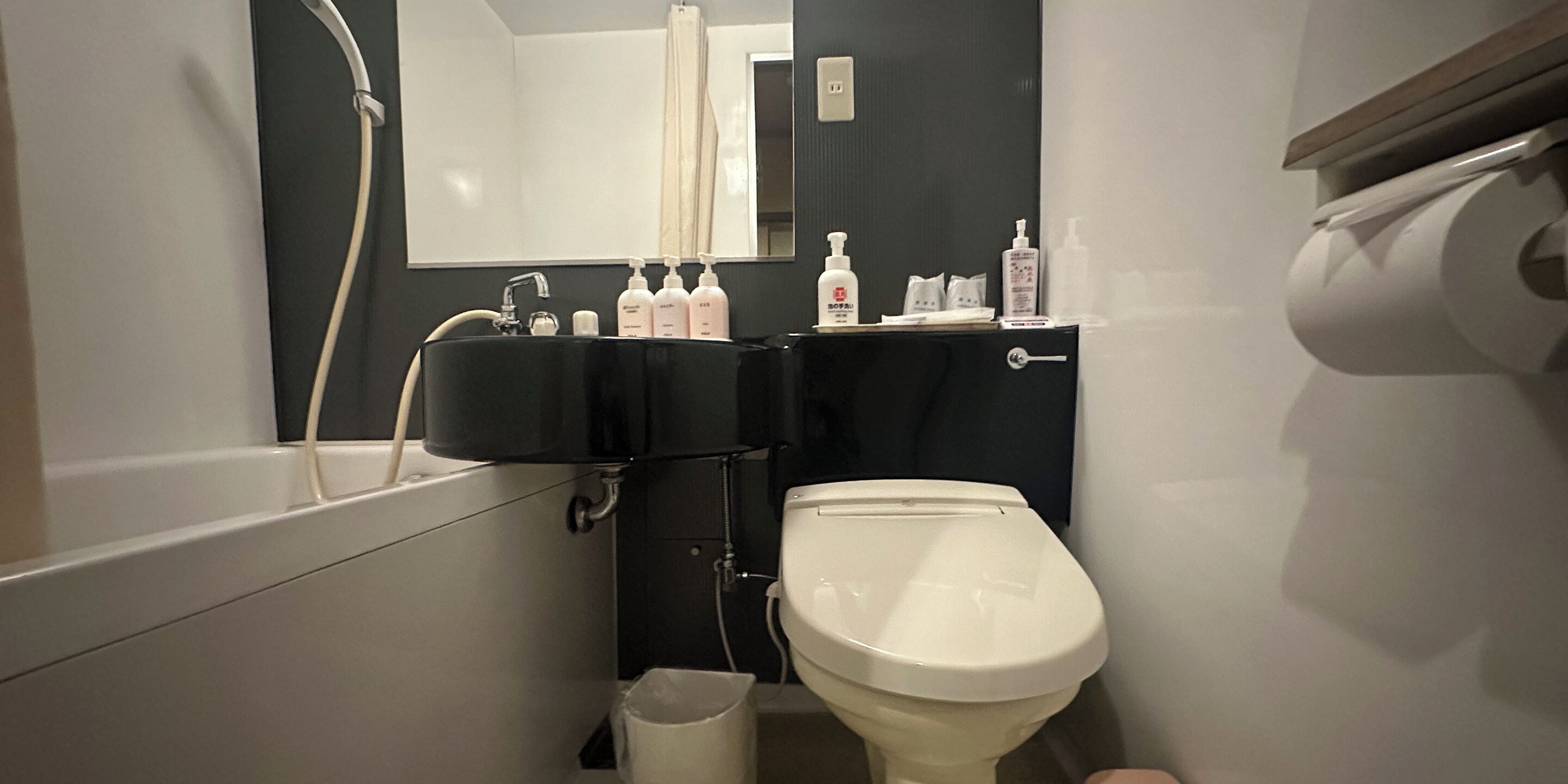 A bathroom with a bathtub, a toilet, and a sink. There are toiletries on the sink and a mirror above it.