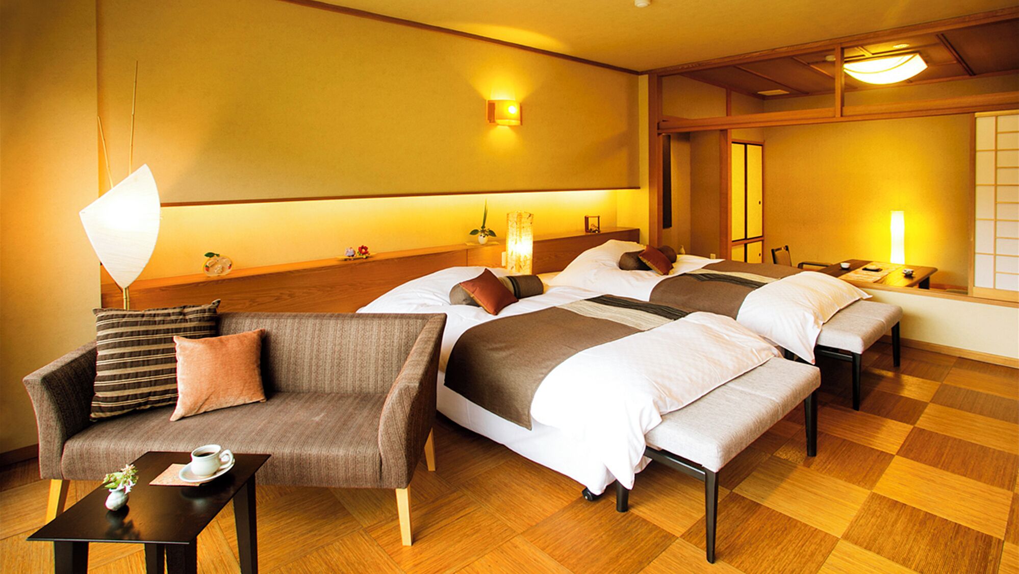 A hotel room with a sofa, two beds, a small table with a cup, and a wooden floor.