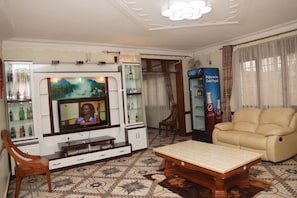 A living room with a television, a sofa, a coffee table, and a Pepsi refrigerator. - Cosmil Executive Suites (Kampala)