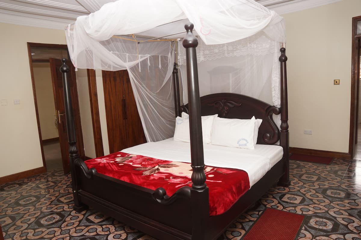 A four-poster bed with a canopy, a red bedspread, and a patterned floor.
