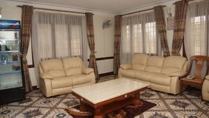 Una sala de estar con dos sofás beige, una mesa de centro de madera, baldosas de suelo con estampado y un refrigerador con bebidas.