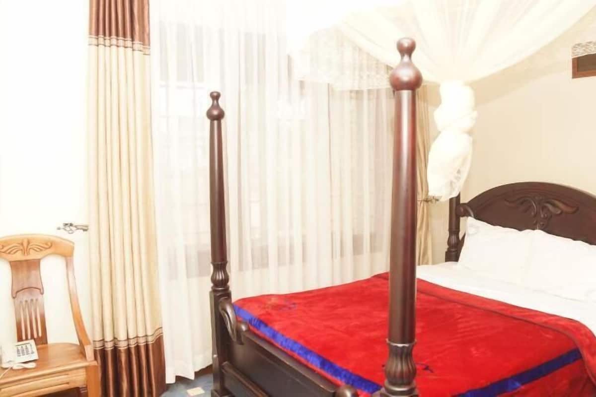 A four-poster bed with a red bedspread, a white pillow, and a wooden headboard.