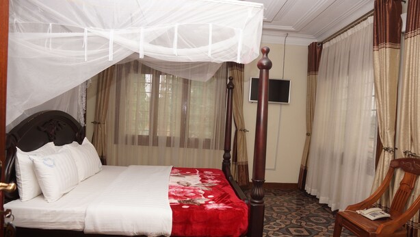 Una cama con dosel y cuatro columnas, una silla de madera y un televisor en la pared.