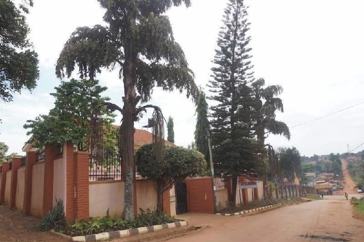 A residential area with a gated entrance, a paved road, and a hilly backdrop.