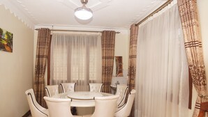 Un comedor con una mesa redonda y seis sillas, rodeado de cortinas estampadas y una lámpara decorativa en el techo.