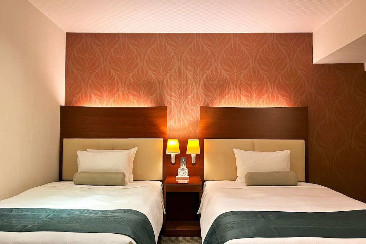 A hotel room with two beds, a wooden headboard, a patterned wallpaper, and two bedside lamps.