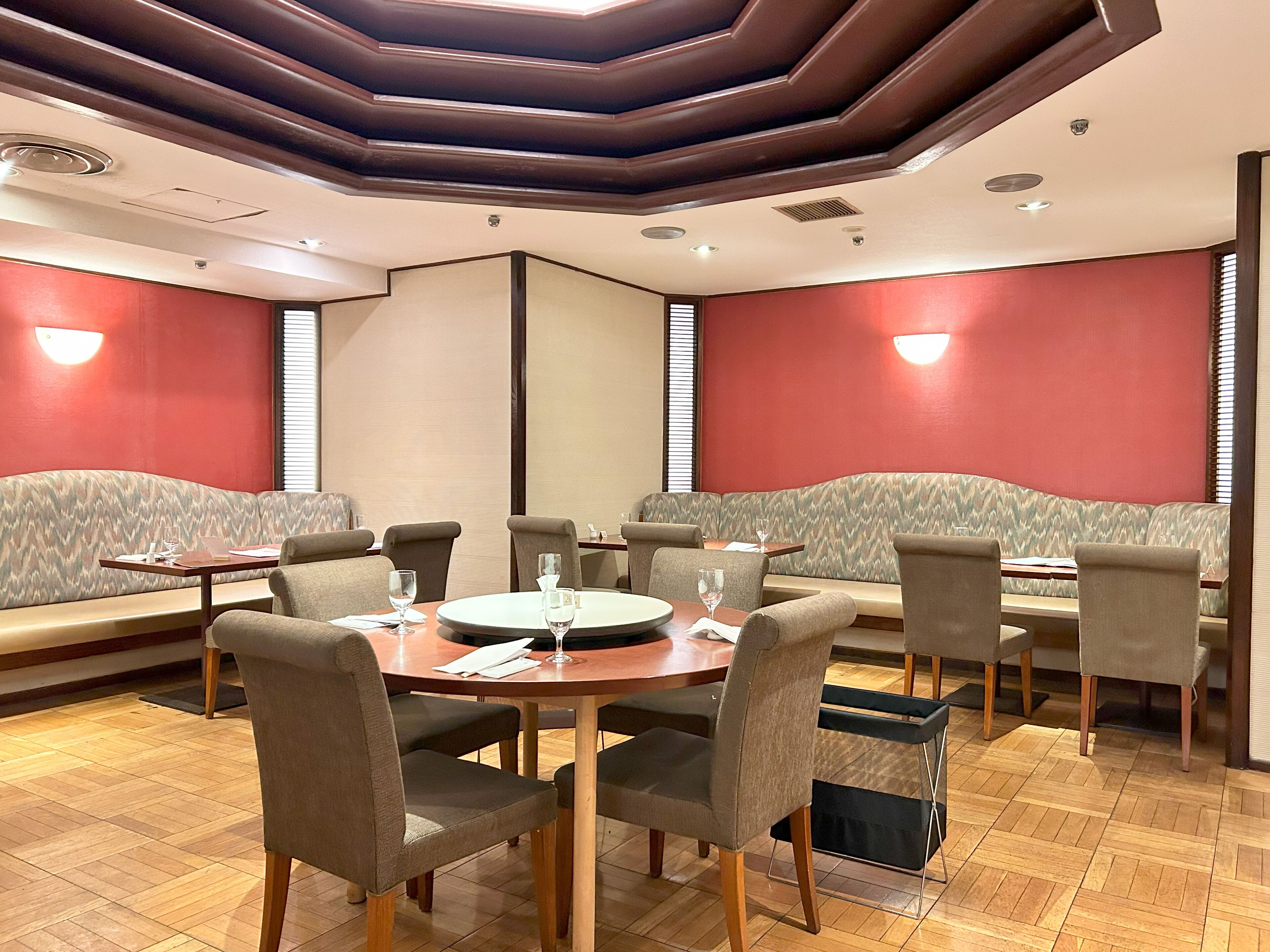 Un comedor con mesas redondas, asientos tapizados y piso de madera.